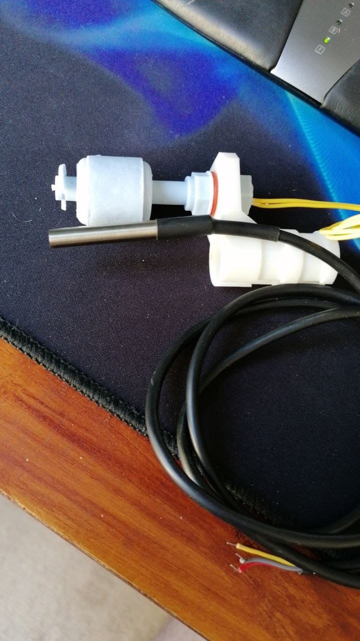 The finished 3D printed bracket on the bench with the float switch fitted and the stainless steel temperature probe alongside it