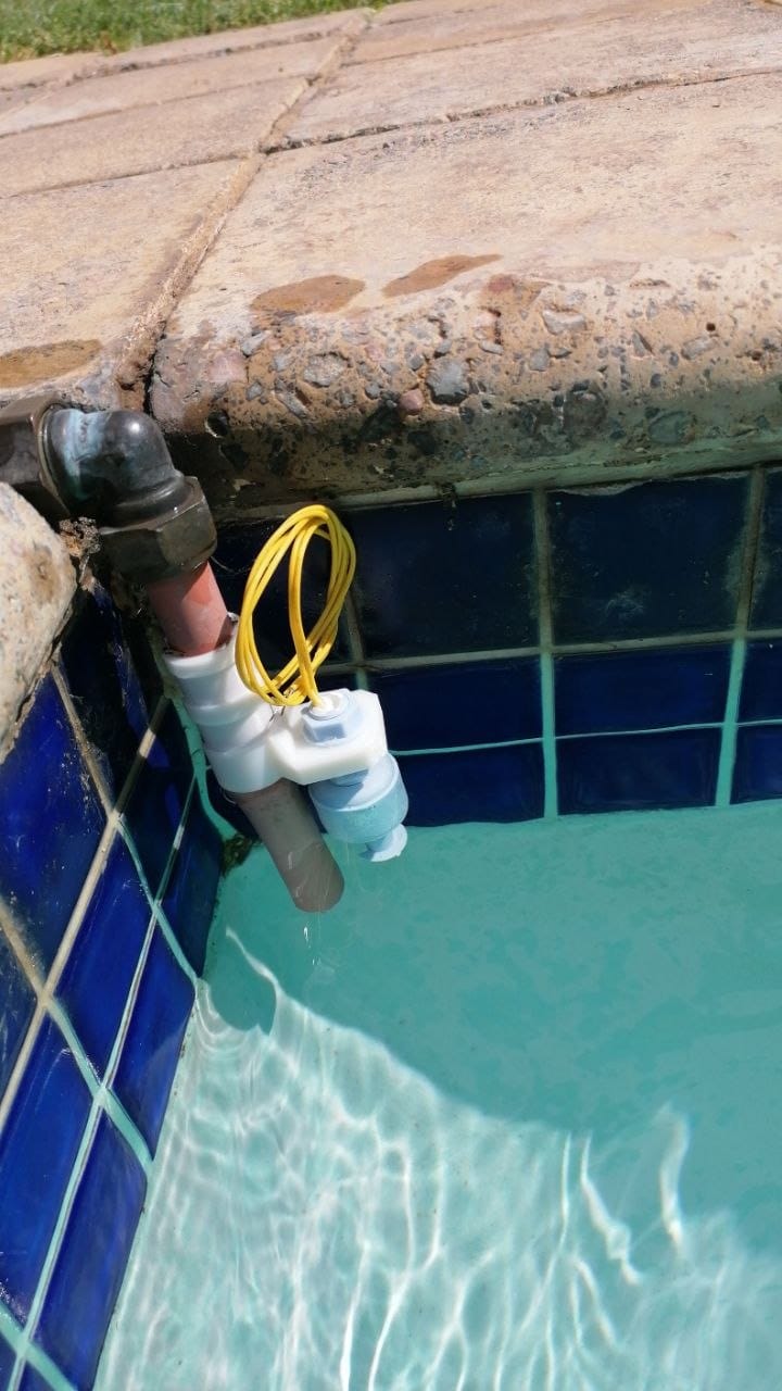 The 3D printed bracket clamped onto the fill pipe at the side of the pool, with the float switch and the probe sitting in the water