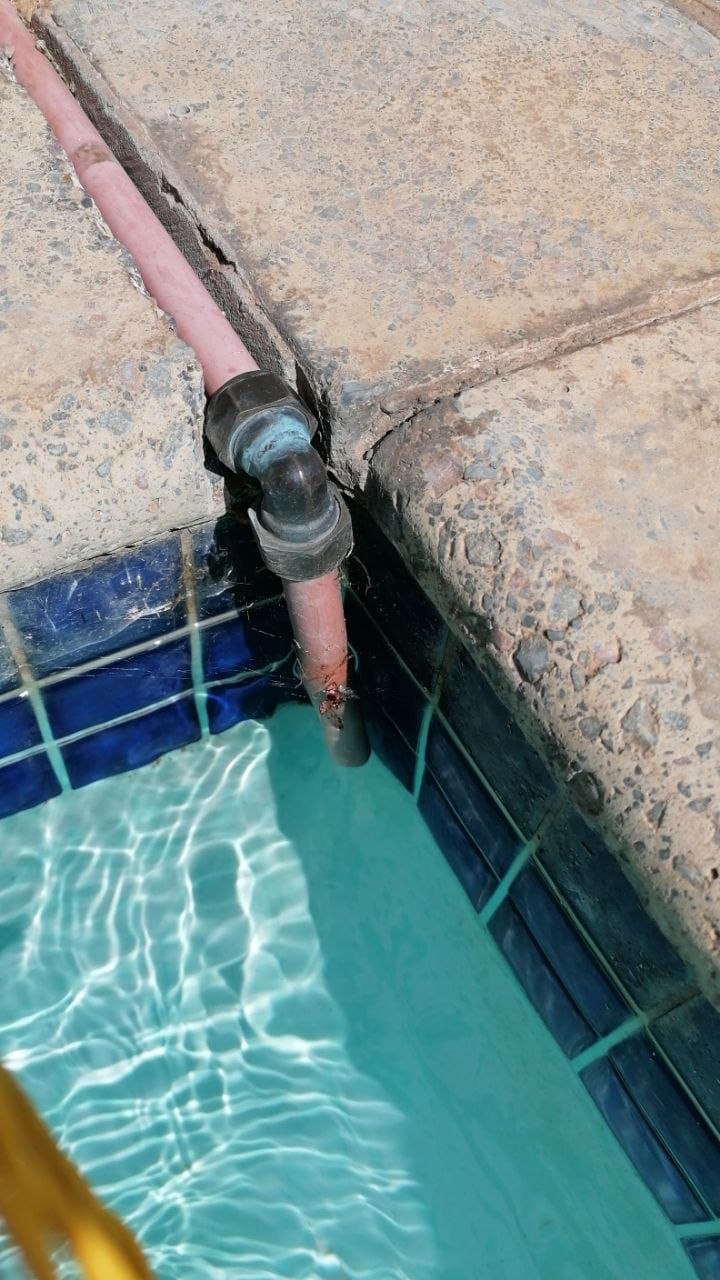 The fill pipe coming through the paving at the edge of the pool with its elbow, and the groove cut into the paving to carry the pipe and the wires