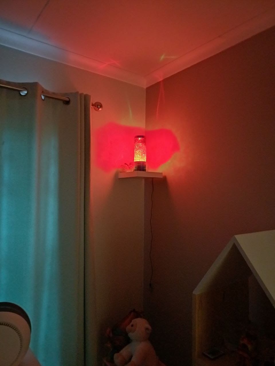 The lamp glowing red on the shelf in her room, with a teddy bear below and the room lit red