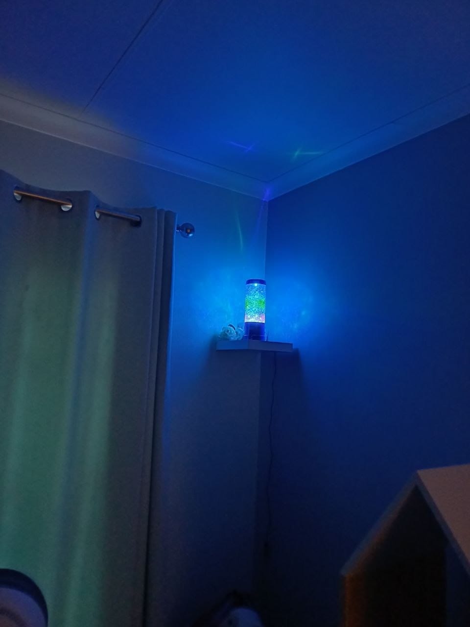 The same lamp glowing blue in the dark bedroom, with the glow washing the corner of the room