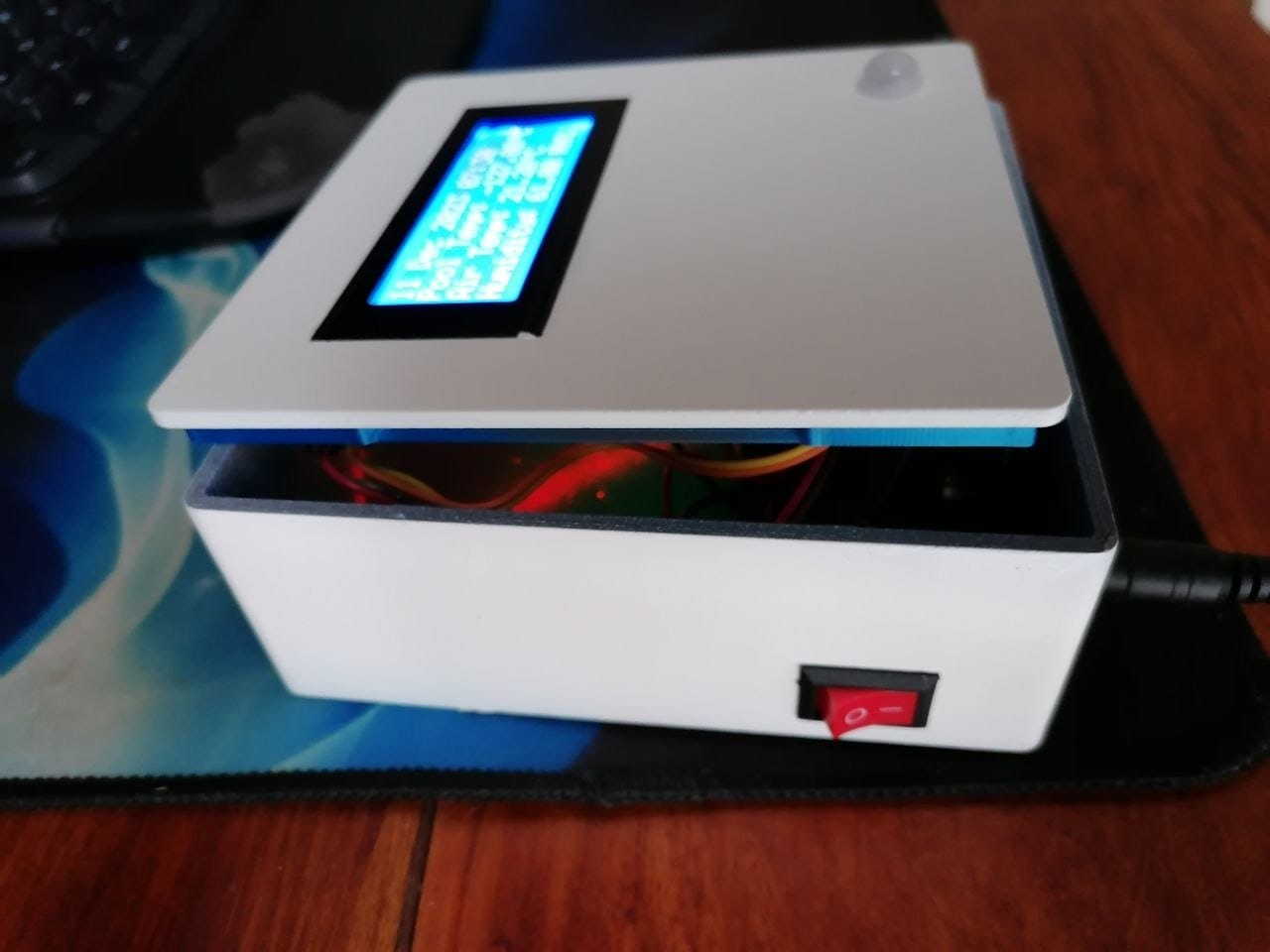 The same painted enclosure from the side, LCD lit and showing readings, the lid sitting slightly open