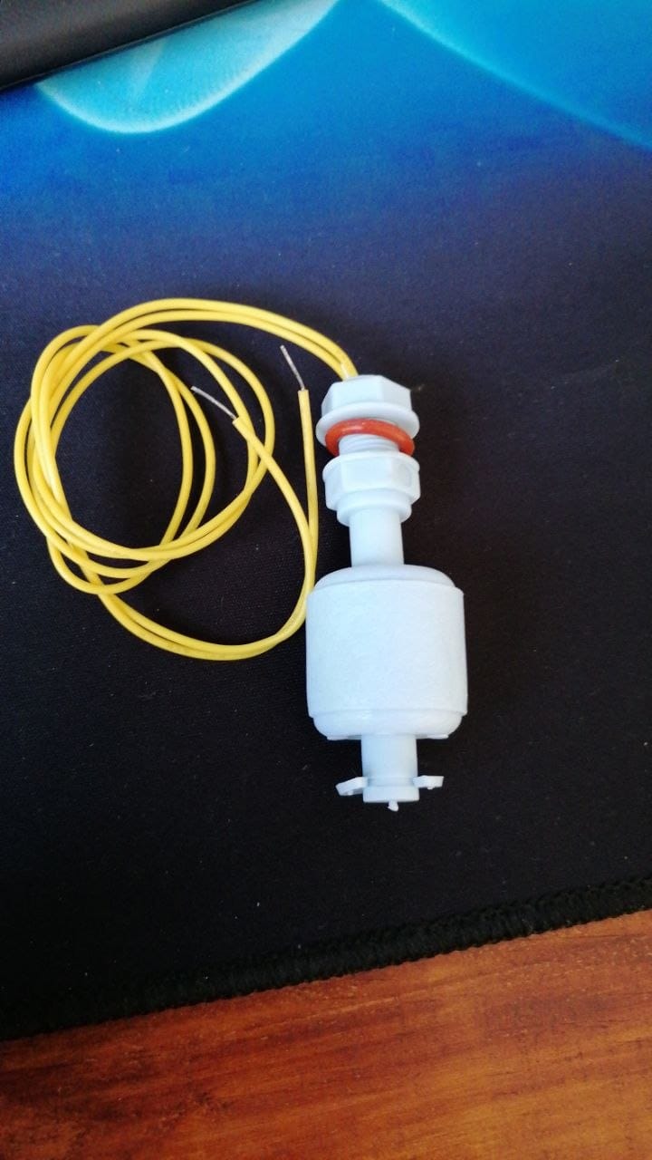 The white float switch on its own on the bench, with its mounting nut, washer and yellow wire