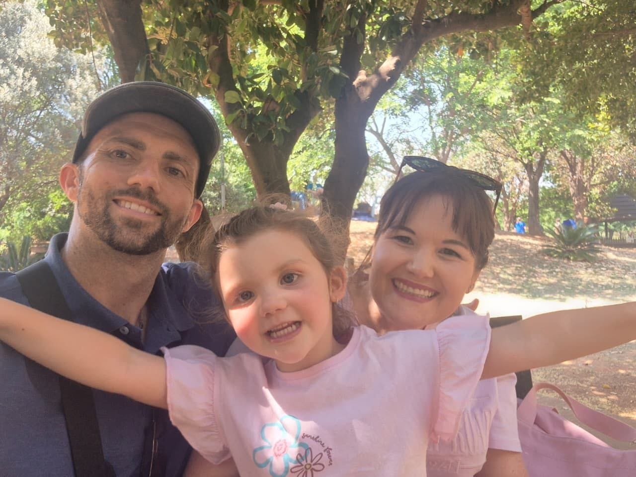 Collin, Ava and Cheryl under the trees, Ava with her arms flung out wide