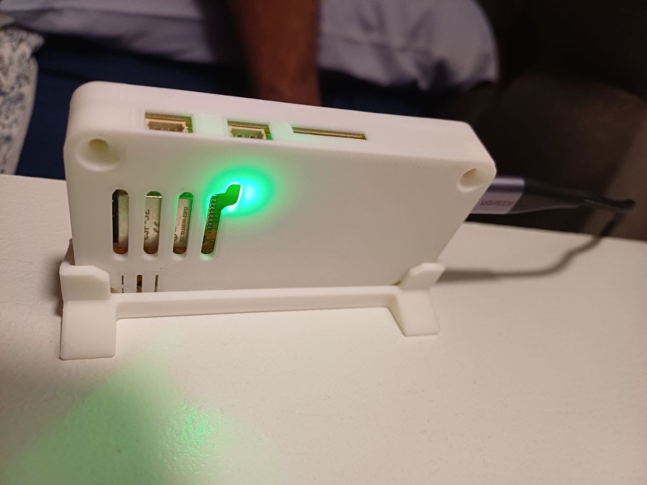 The back of the bedside display showing the white 3D-printed enclosure, a bright green status LED, ventilation slots and exposed GPIO pins