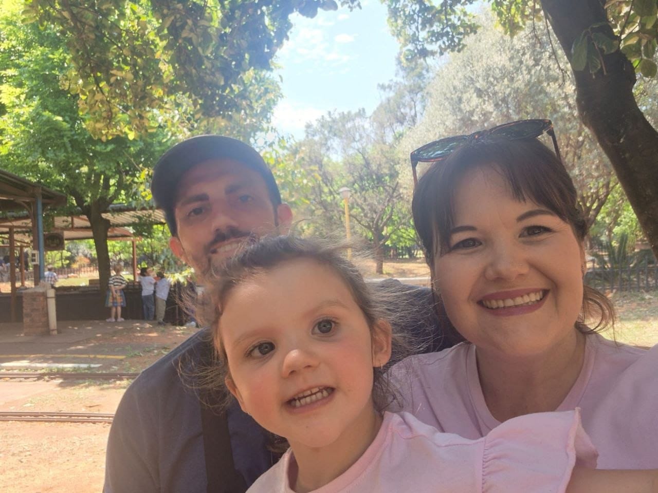Family selfie of Collin, Ava and Cheryl under the trees with the station canopy and the track behind them