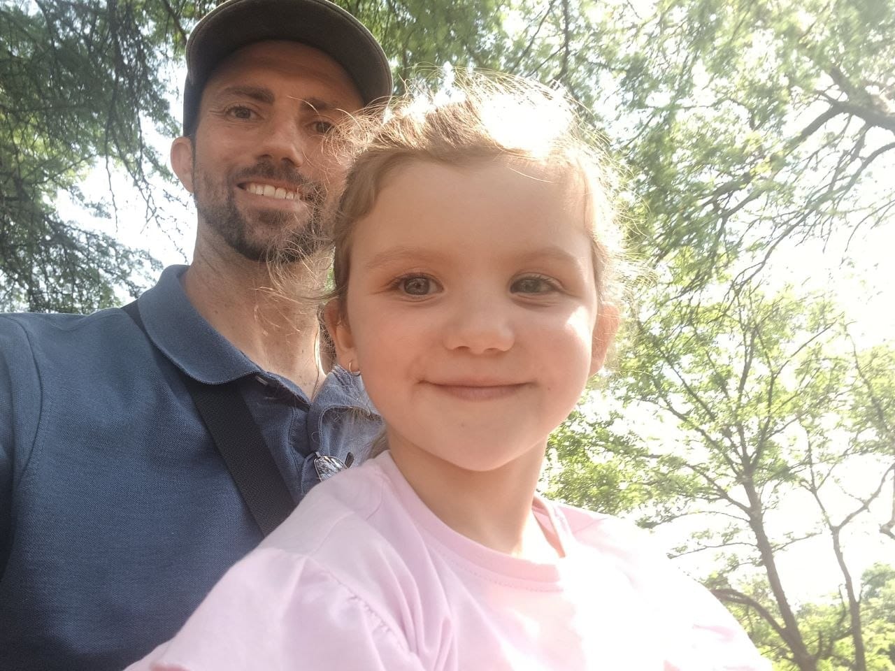 Selfie of Collin and Ava backlit by sunlight through the trees