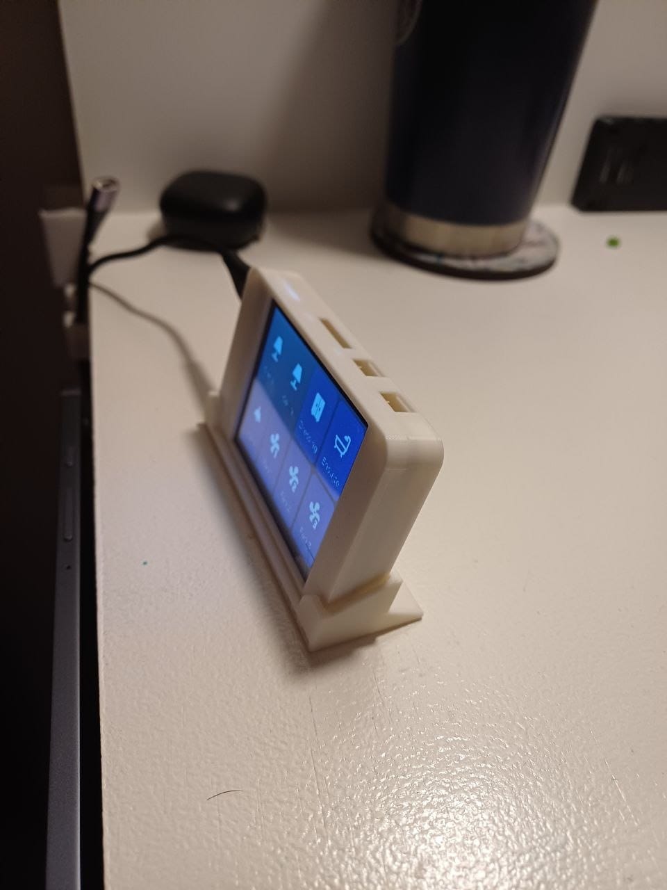 The bedside display seen from an angle on its 3D-printed stand, the tile grid visible on screen with the Dressing, Ensuite and fan tiles lit blue