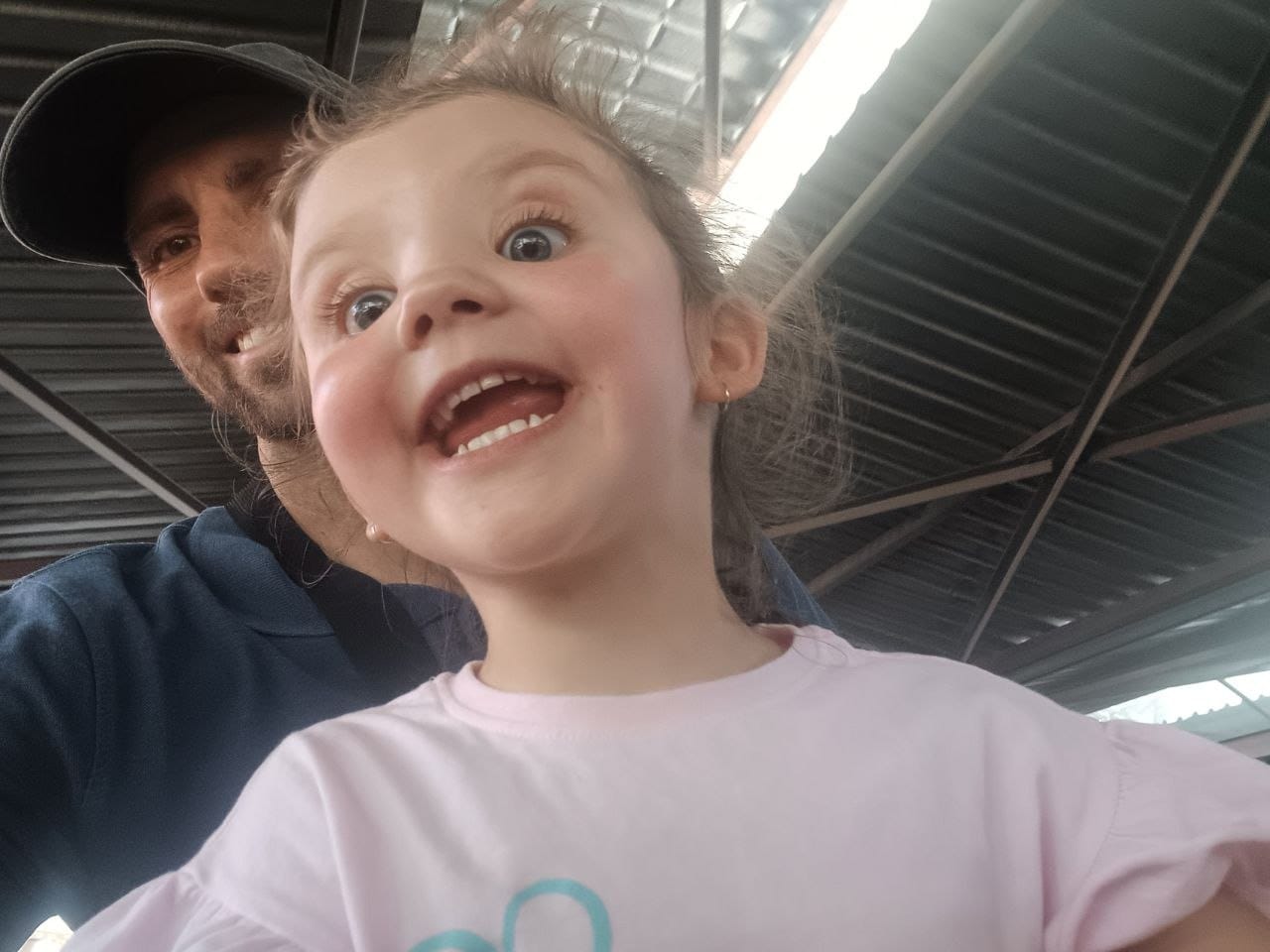 Ava beaming up at the camera under the station canopy with Collin behind her